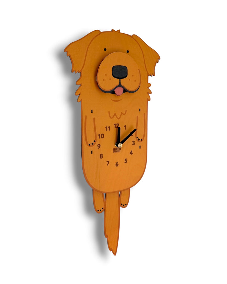 A golden retriever wall clock made from layered orange-brown wood, featuring a cartoon dog face and black clock hands on a plain white background.